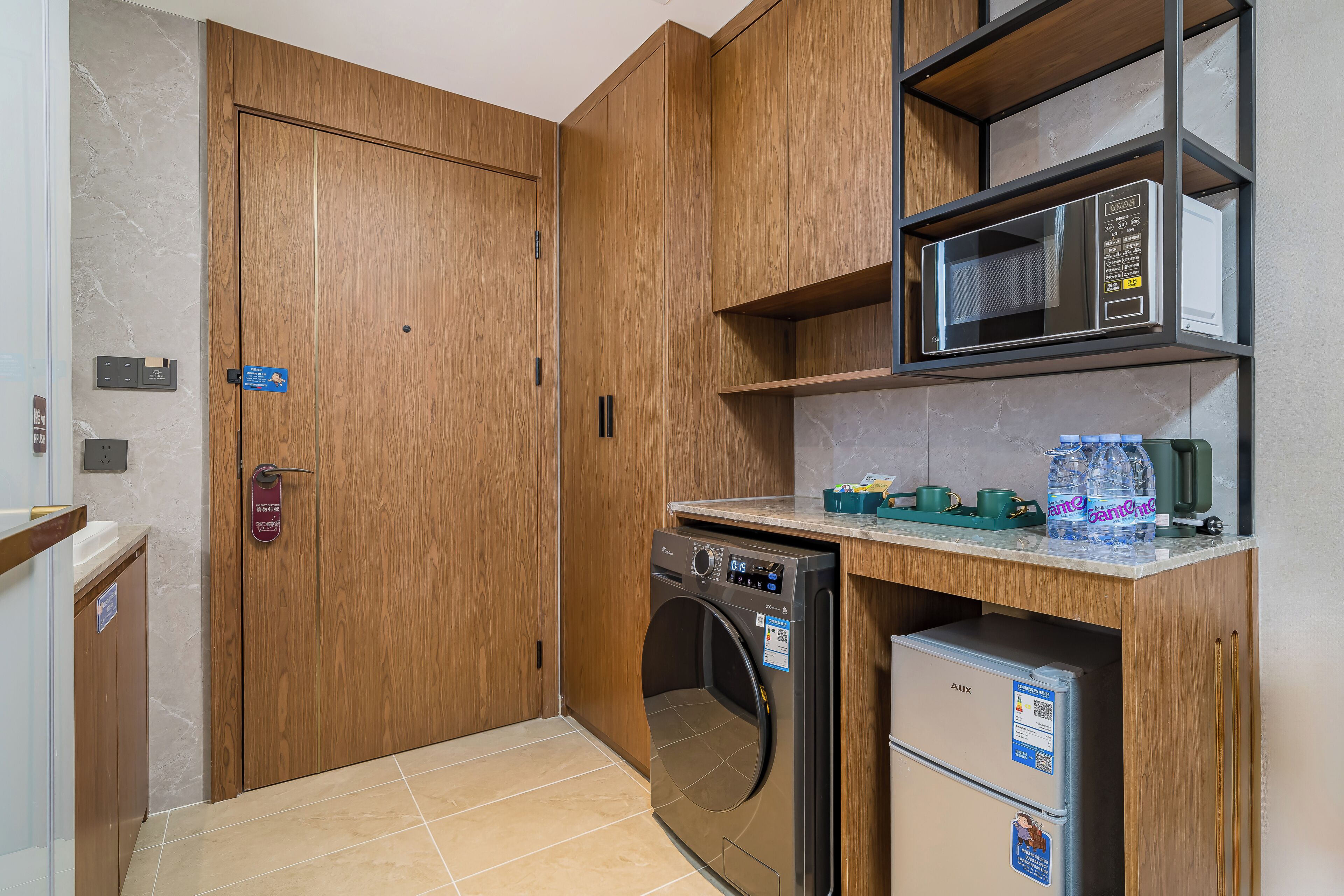 A compact kitchen with wooden cabinetry, a built-in washing machine, a microwave, and a small refrigerator.