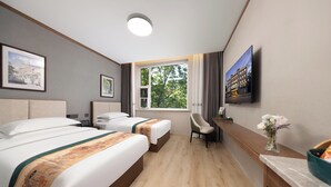 Hotellihuone, jossa on kaksi sänkyä, työpöytä, tuoli, televisio ja ikkuna, jossa on verhot.