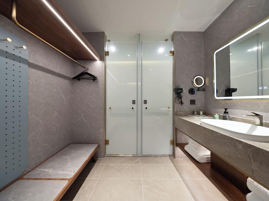 A modern bathroom with a glass shower enclosure, a large mirror, and a marble countertop.