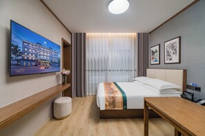 A hotel room with a bed, a desk, a TV, and a window with curtains.