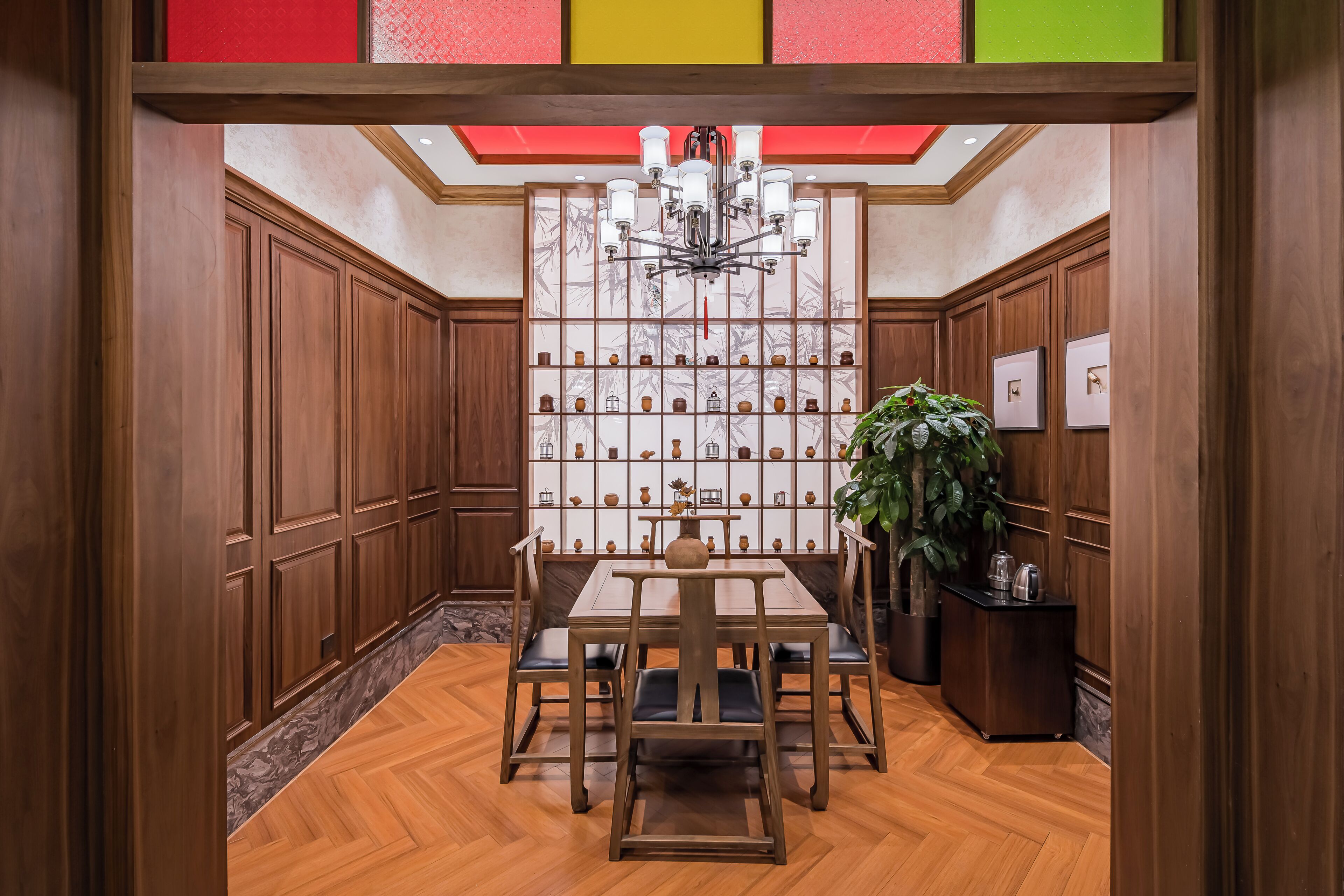 A dining area with a wooden table and chairs, a chandelier, a wall of decorative vases, and a potted plant.