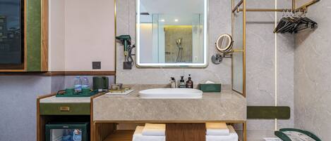 A modern bathroom with a marble sink, a large mirror, a towel rack, and a small refrigerator.