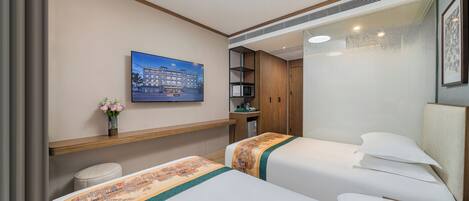 A hotel room with two beds, a small stool, a shelf with a vase of flowers, a painting on the wall, and a microwave in the corner.