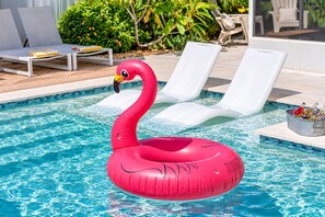 Ein Swimmingpool mit einem rosa Flamingo-Schwimmding, Liegestühlen und einem Eimer mit Flaschen.