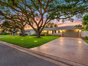 A residential house with a driveway, a garage, and a large tree in the front yard.