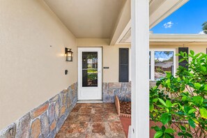 A covered porch with a stone wall, a door, and a small seating area with a planter.