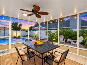 A patio area with a pool, dining table, chairs, and a ceiling fan.
