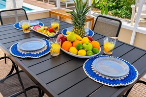 Ein Essplatz im Freien mit blau-weißen Häkel-Untersetzern, Obst und Gläsern Orangensaft.