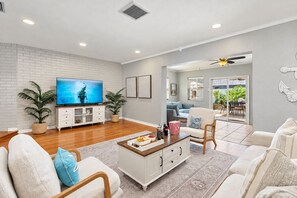 A living room with a television, seating, a coffee table, and a view to an outdoor area. - Captivating Brand-New Heated Pool in Seminole | 5 Mins to Beaches (Seminole)