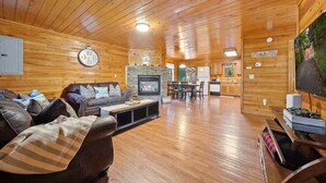 A cozy cabin interior with a fireplace, wooden walls, a dining area, and a kitchen. - Cozy Cabin w/ Hot Tub – Sleeps 8 Comfortably (Pigeon Forge)