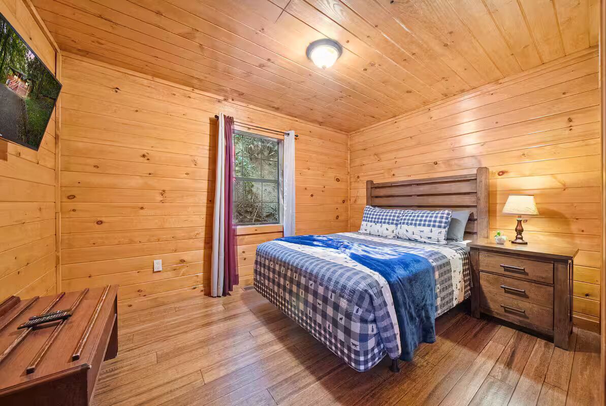 A wooden cabin bedroom with a bed, bedside table, and a window with curtains.