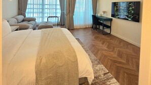 Ruime slaapkamer met een groot bed, een bureau, een stoel, een kroonluchter en een groot raam met gordijnen.