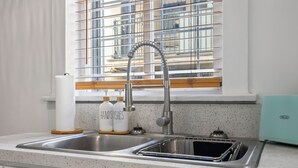 A kitchen with a stainless steel sink, a window with blinds, and a BELLA toaster. - Updated Studio in Downtown Long Beach - Walk to Everything (Long Beach)