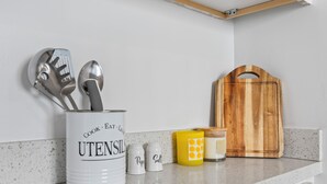 A kitchen counter with a white utensil canister labeled "Cook Eat Live Utensils," two salt and pepper shakers, a yellow mug with a geometric pattern, and a wooden cutting board. - Updated Studio in Downtown Long Beach - Walk to Everything (Long Beach)