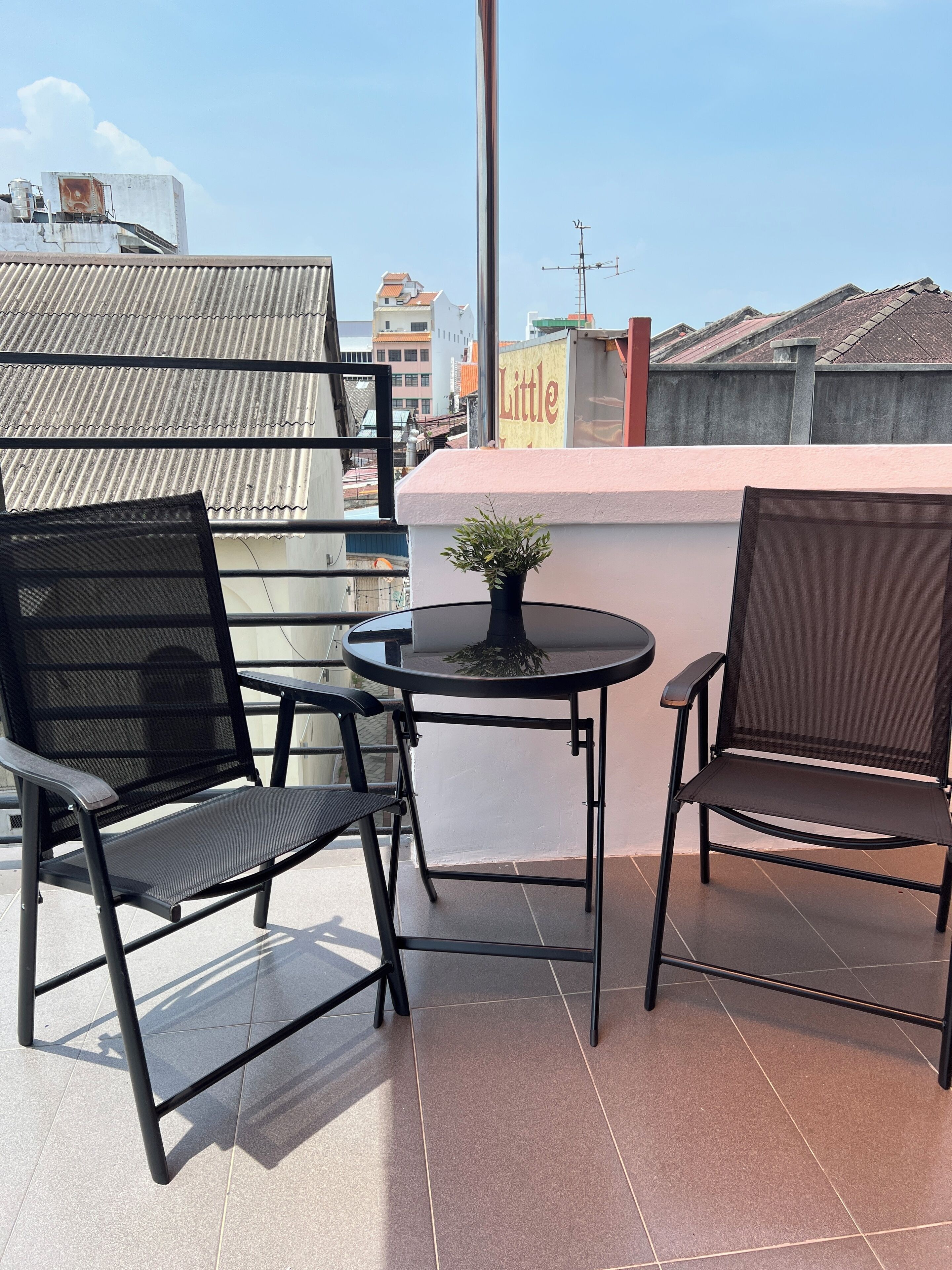 Un pequeño espacio al aire libre con dos sillas, una mesa, una planta en maceta y vistas a la ciudad.