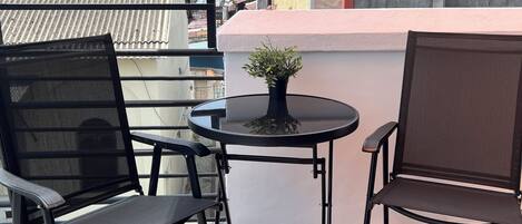 Un pequeño espacio al aire libre con dos sillas, una mesa, una planta en maceta y vistas a la ciudad.