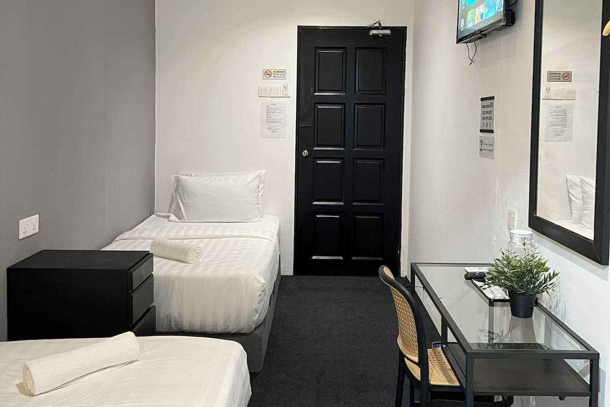Ein Hotelzimmer mit zwei Betten, einem Schreibtisch mit Stuhl, einem Fernseher und einem Spiegel.