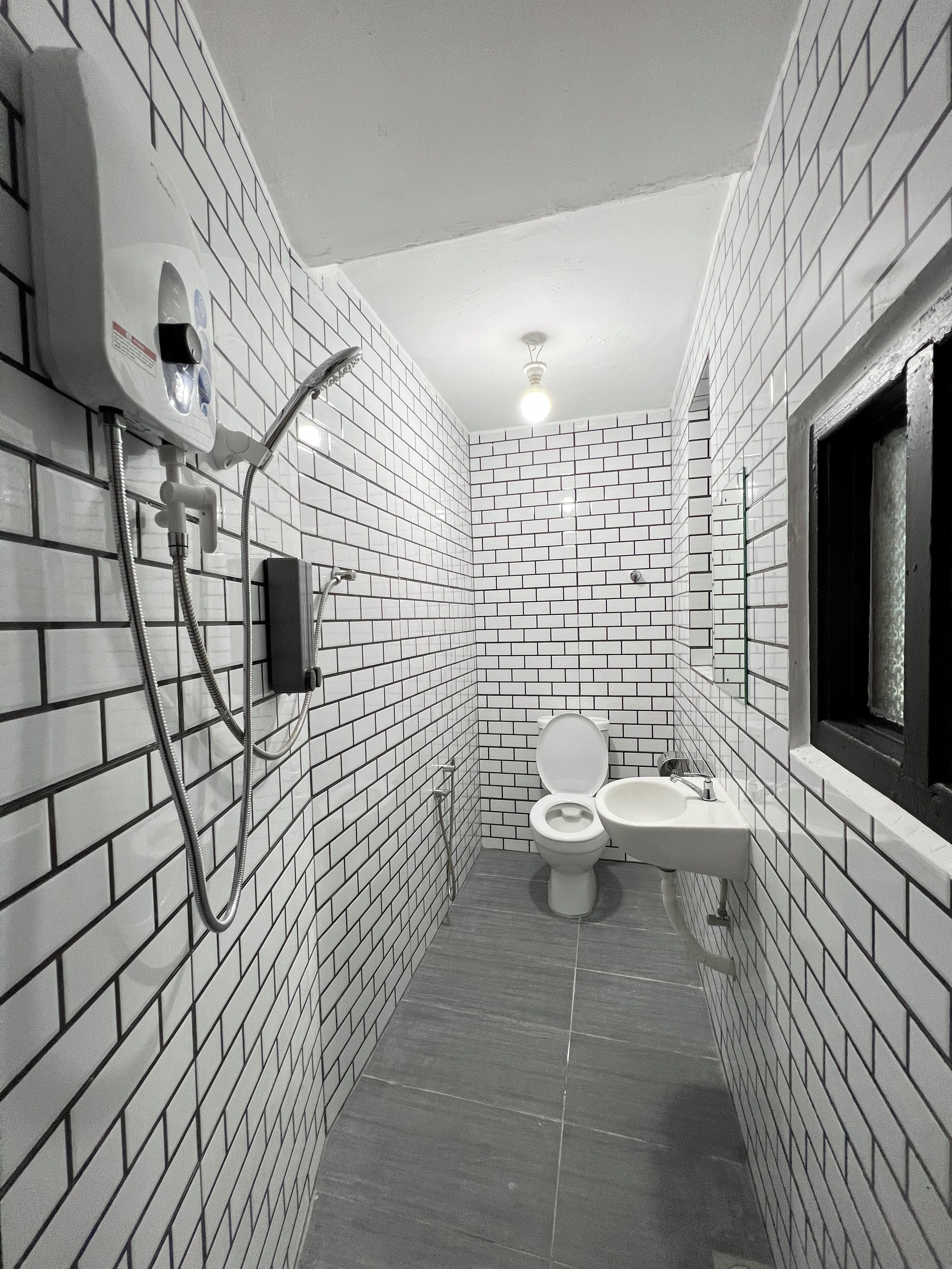 A bathroom with white tiled walls and floor, a toilet, a sink, and a shower with a handheld showerhead.