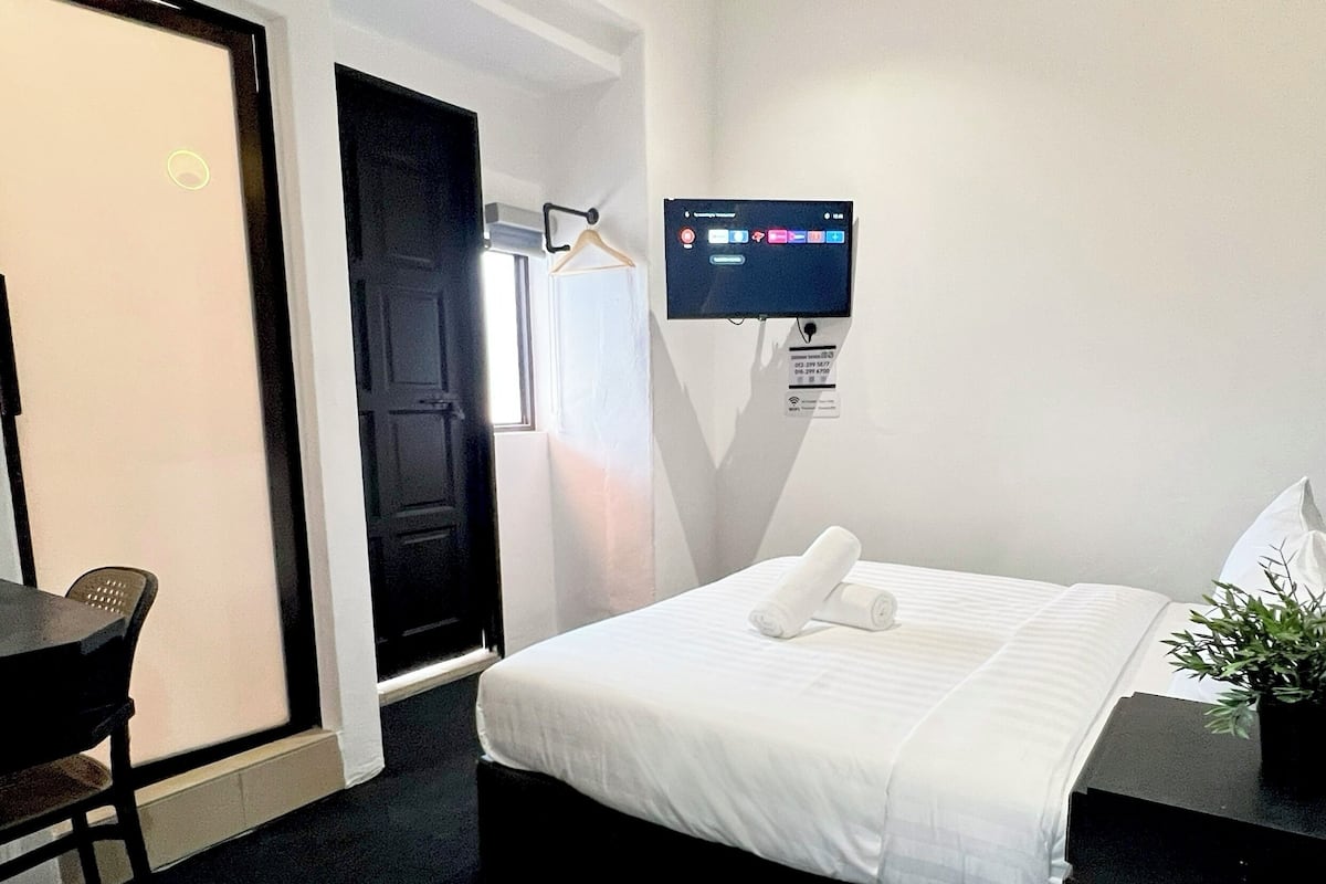 Ein Hotelzimmer mit einem Bett, einem Schreibtisch, einem Sessel, einem Deckenventilator und einem an der Wand befestigten Fernseher.