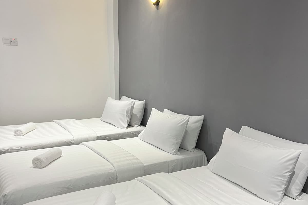 Ein Hotelzimmer mit zwei Einzelbetten, jeweils mit weißer Bettwäsche und Kissen, einem Deckenventilator und einer wandmontierten Lampe.