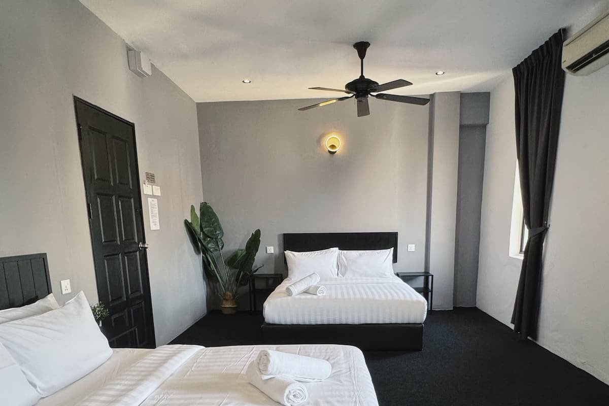 Ein Hotelzimmer mit zwei Betten, einem Deckenventilator, einer Topfpflanze und einem Fenster mit Vorhängen.