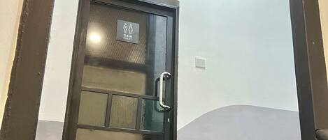 Puerta negra con un panel de vidrio y una barandilla, que da a una zona con baldosas y escalones.
