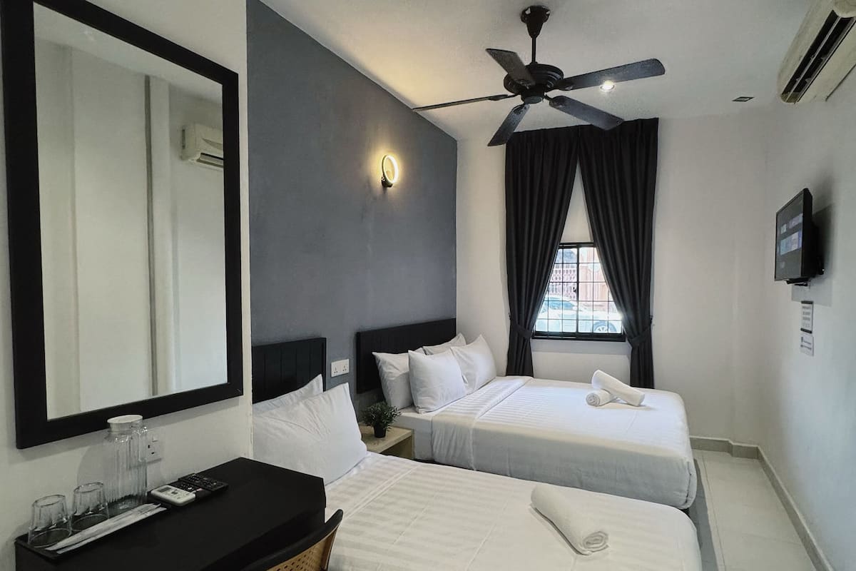 Ein Hotelzimmer mit zwei Betten, einem Schreibtisch mit Stuhl, einem Deckenventilator und einem Fernseher an der Wand.