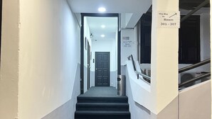A clean, well-lit hallway with a carpeted staircase leading to a door. There are signs indicating room numbers 301-307. - Quee Hotel (George Town)