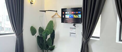 Una habitación de hotel con cama, televisor, planta en maceta y ventana con cortinas.