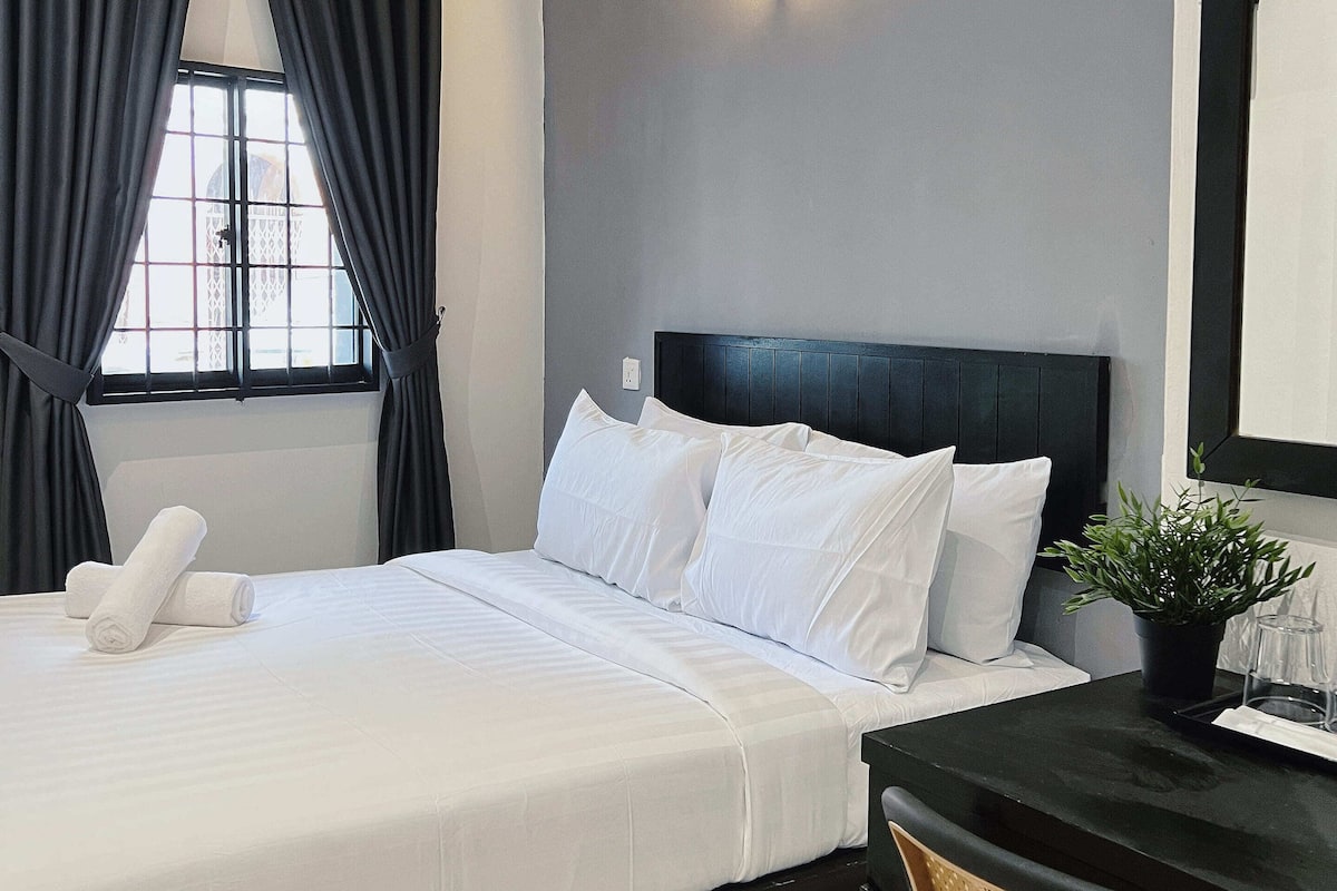 Ein Hotelzimmer mit Bett, Schreibtisch, Stuhl, Topfpflanze und Klimaanlage.
