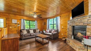 Un intérieur de chalet chaleureux avec une cheminée en pierre, un plafond en bois et un ensemble de canapés en cuir.