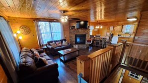 Un intérieur de chalet chaleureux comprenant un salon, une cheminée, un coin repas et une cuisine.