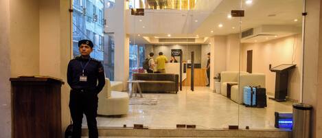 A hotel lobby with a reception desk, seating area, and a view of the outside buildings.