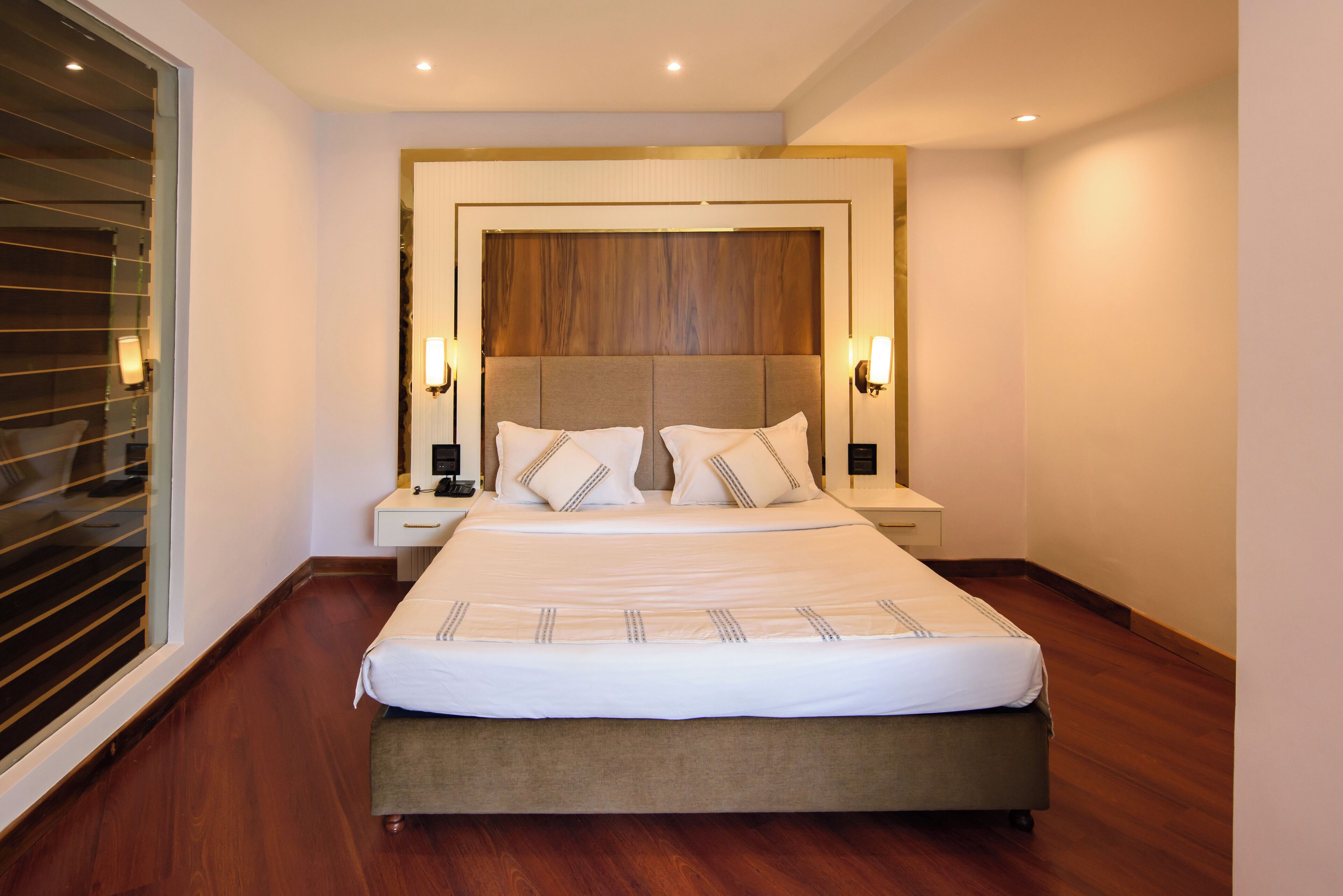 Ein ordentlich eingerichtetes Hotelzimmer mit einem großen Bett, Nachttischen und einem Fenster mit Jalousien.