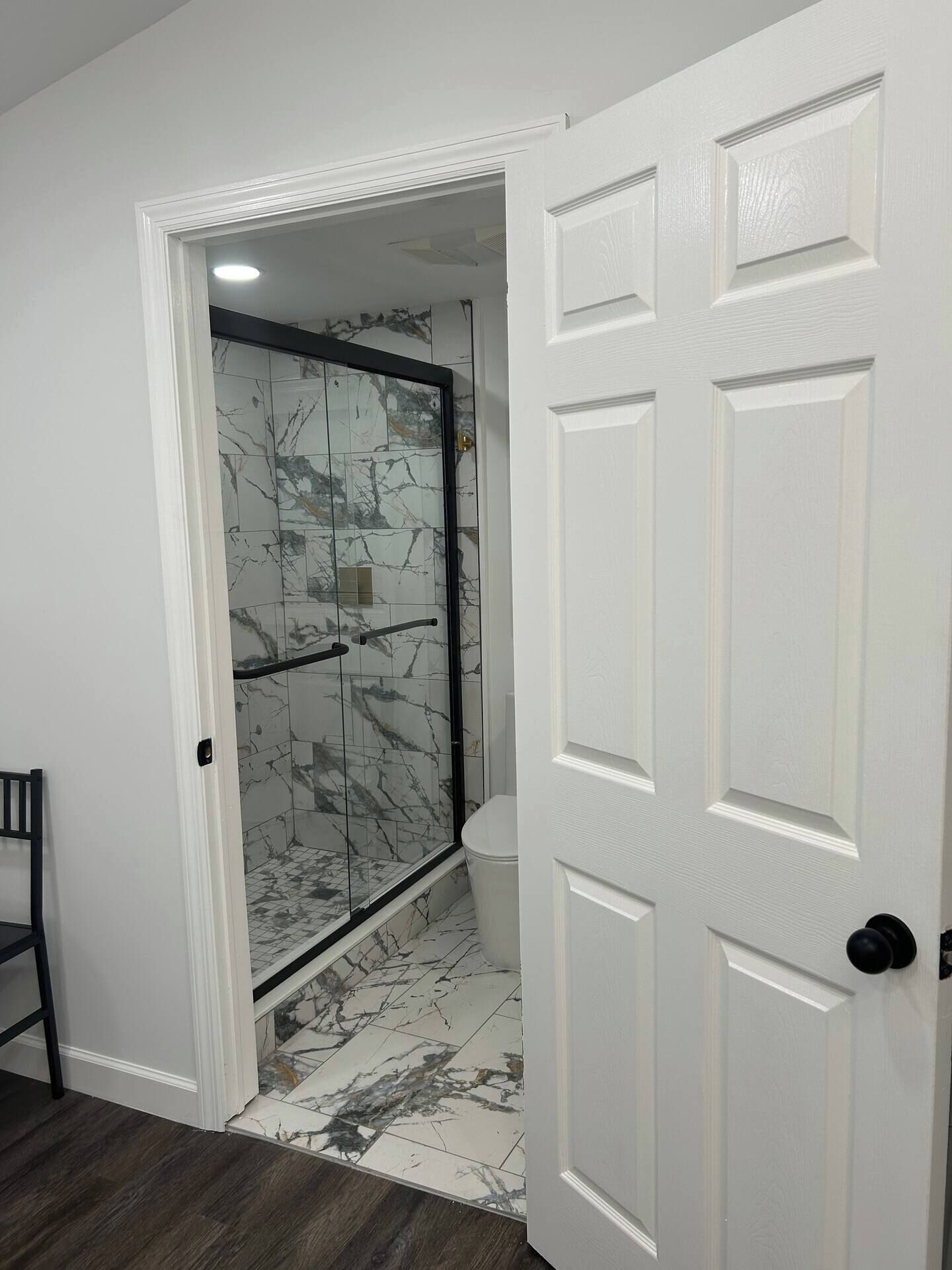 Une salle de bain avec une porte de douche en verre, des toilettes et un plancher en bois.