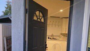 Une porte qui donne sur une cuisine avec des meubles blancs, une chaise blanche et un plancher en bois.