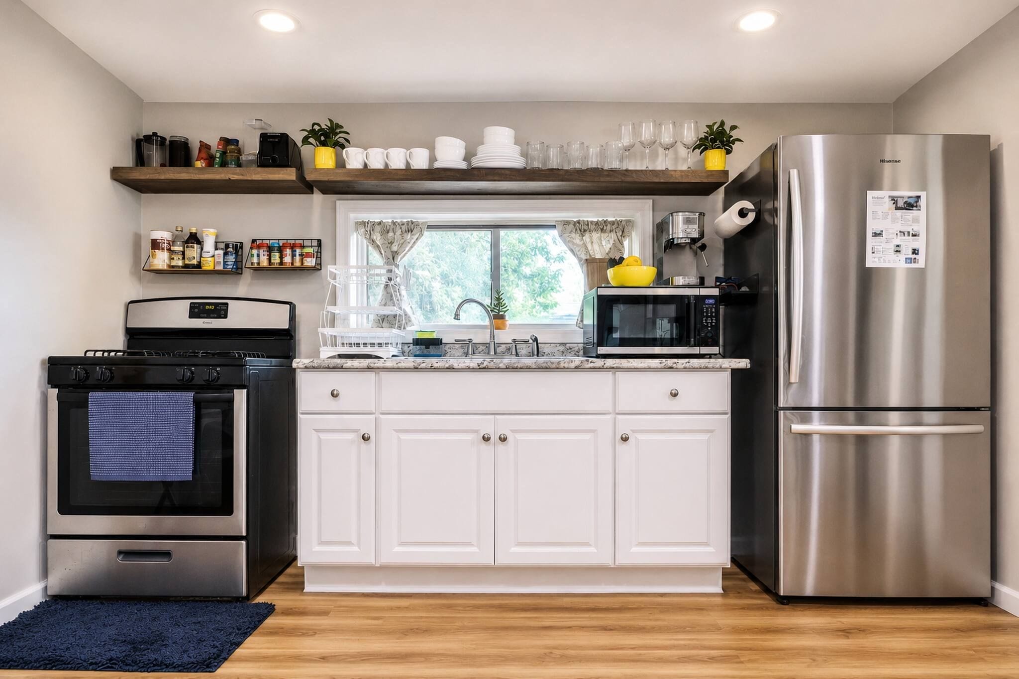 A modern kitchen with white cabinets, stainless steel appliances, and a window with curtains.