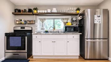 A modern kitchen with white cabinets, stainless steel appliances, and a window with curtains.