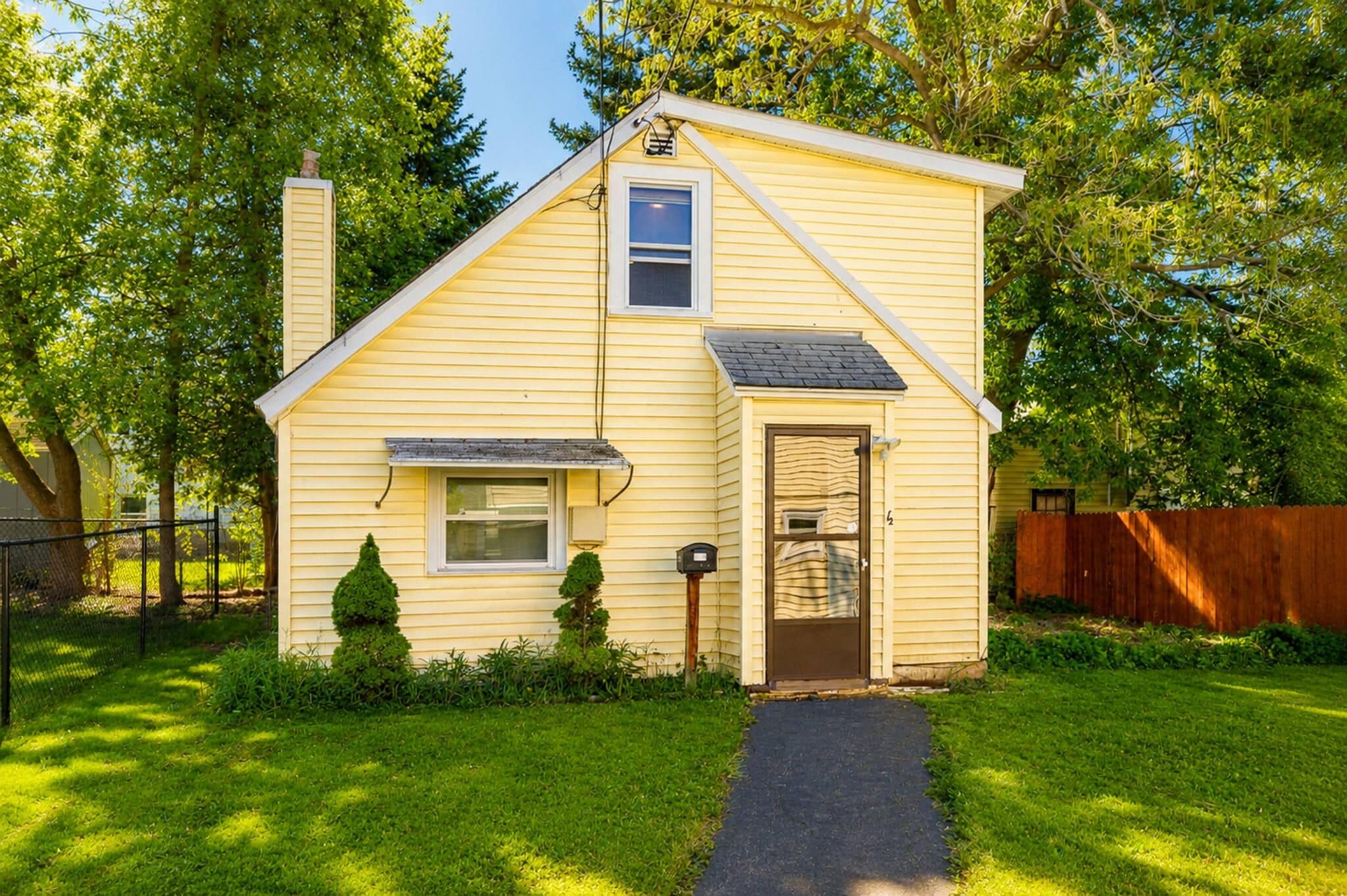 A single-story yellow house with a front door, a small window, a chimney, and a mailbox.