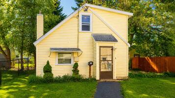 A single-story yellow house with a front door, a small window, a chimney, and a mailbox.
