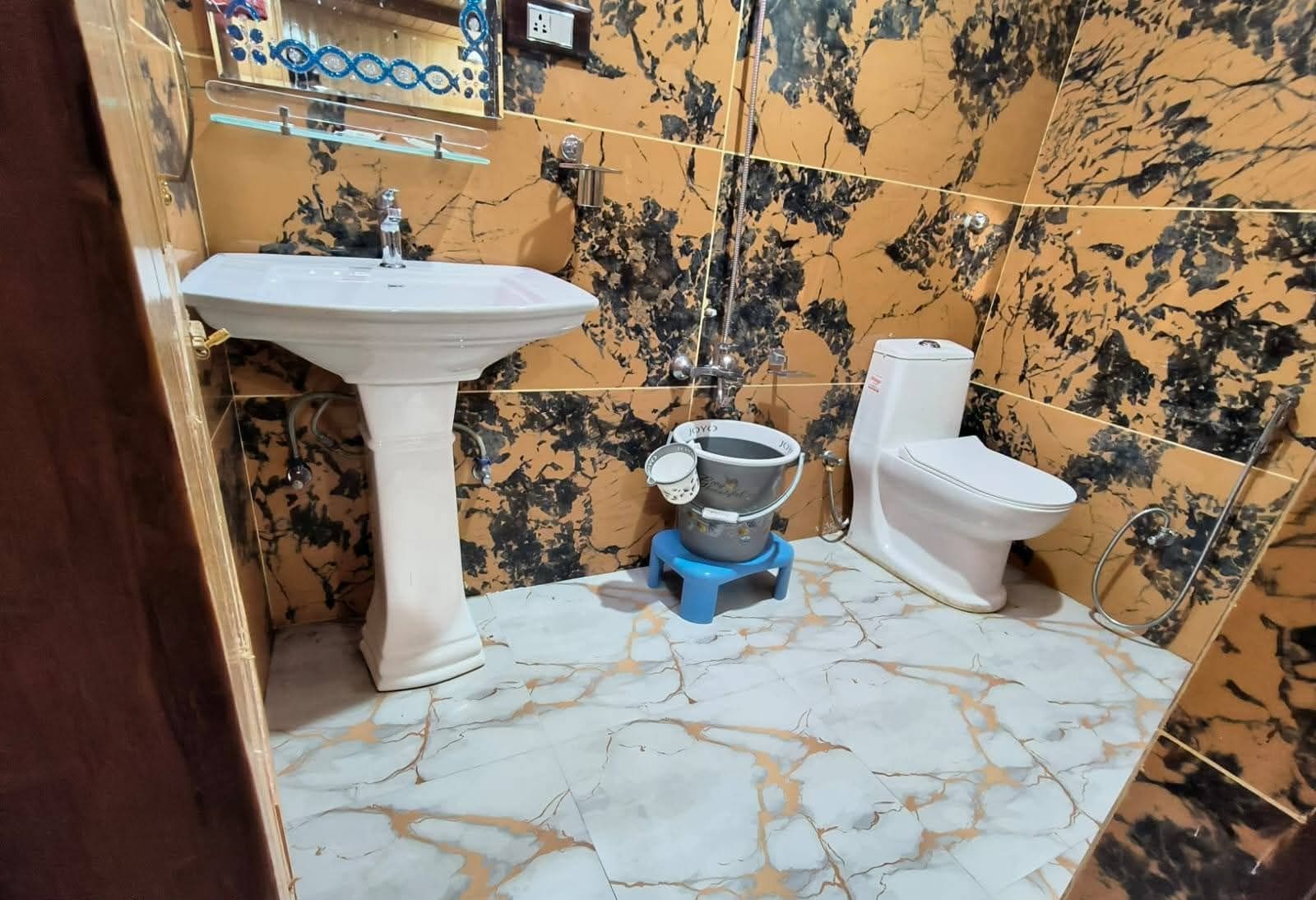 A bathroom with a pedestal sink, toilet, and a small blue stand-up shower unit.