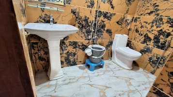 A bathroom with a pedestal sink, toilet, and a small blue stand-up shower unit.