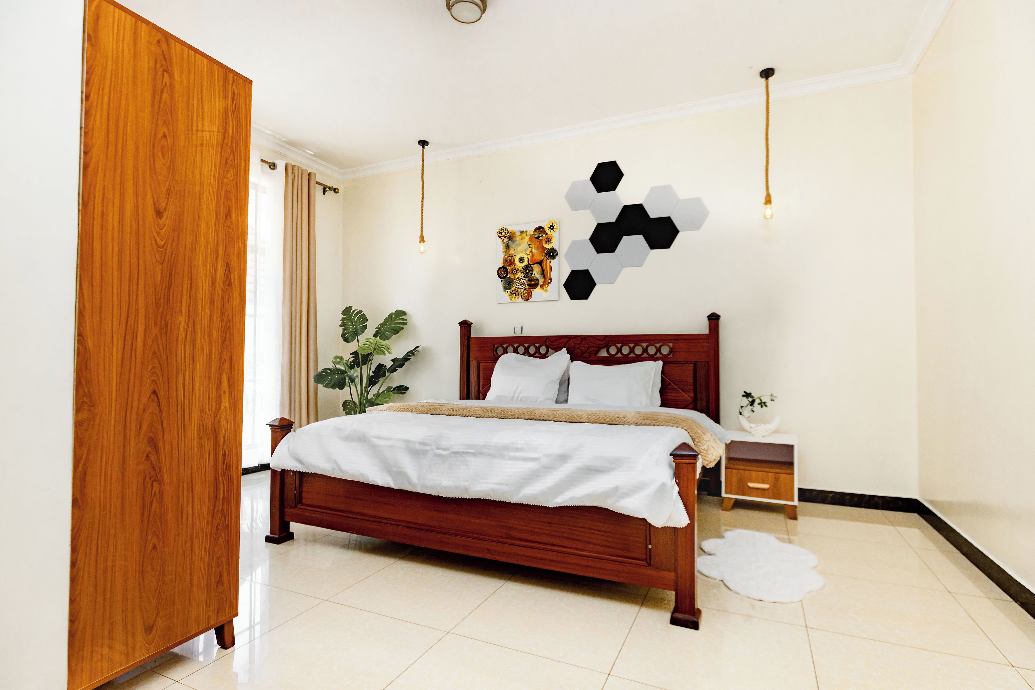 A bedroom with a wooden bed, a nightstand, a wall art piece, and a potted plant.
