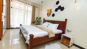 A neatly made bed with a wooden headboard, a bedside table with a drawer, a potted plant, and a wall art piece.