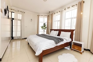 Une chambre à coucher moderne avec un grand lit, une table de chevet, une commode et une plante en pot.