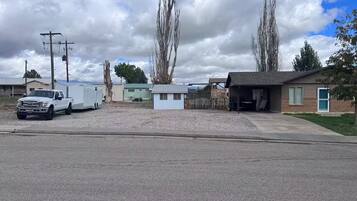 A residential area with a white pickup truck parked on a gravel driveway, a small house with a garage, and a fenced yard.