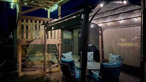 A covered outdoor seating area with a wooden deck, a glass enclosure, and string lights.