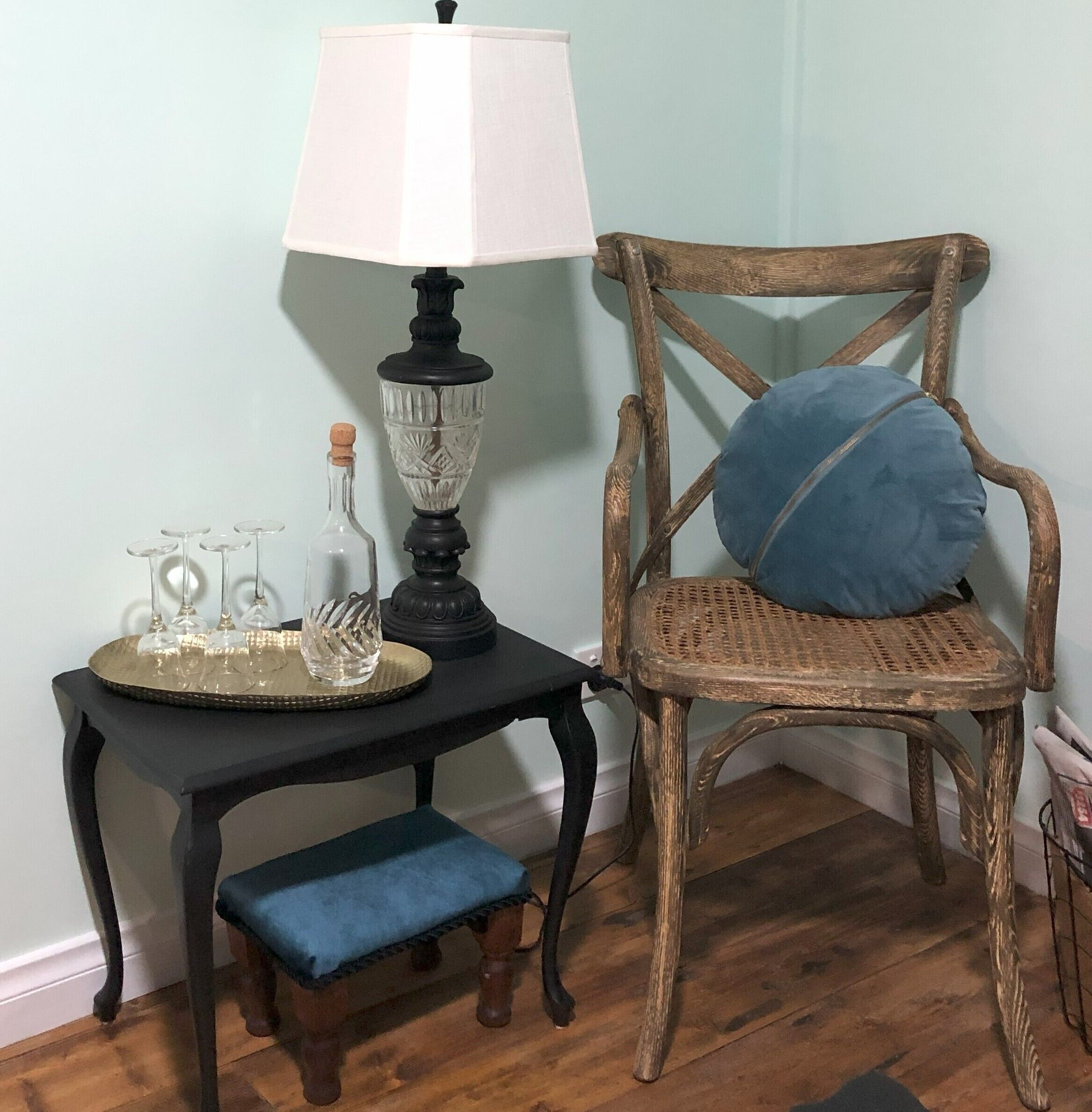 Une chaise en bois avec un coussin bleu, une petite table avec une lampe et un plateau avec des verres et une bouteille.
