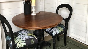 Una mesa redonda de madera con sillas, un espejo, una vela y un florero con ramas.