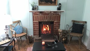 Una sala de estar acogedora con chimenea, dos sillones de madera, una mesa con vela y un cuadro en la pared.